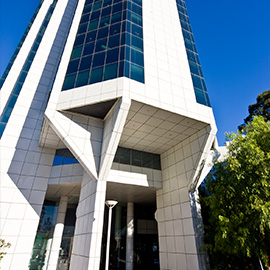 Entrance of a tall, white office building with a blue sky in the background. 